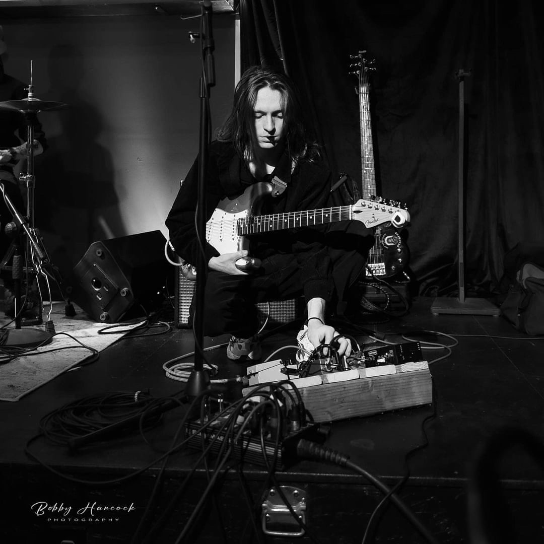 A black and white picture of my kneeling on stage to change the effects on my pedalboard.